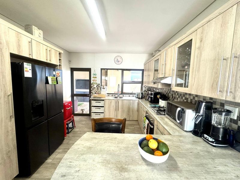 A functional kitchen featuring light wood-look cabinetry, stone-effect countertops, a tiled backsplash, and integrated cooking appliances with direct access to the rear exterior.