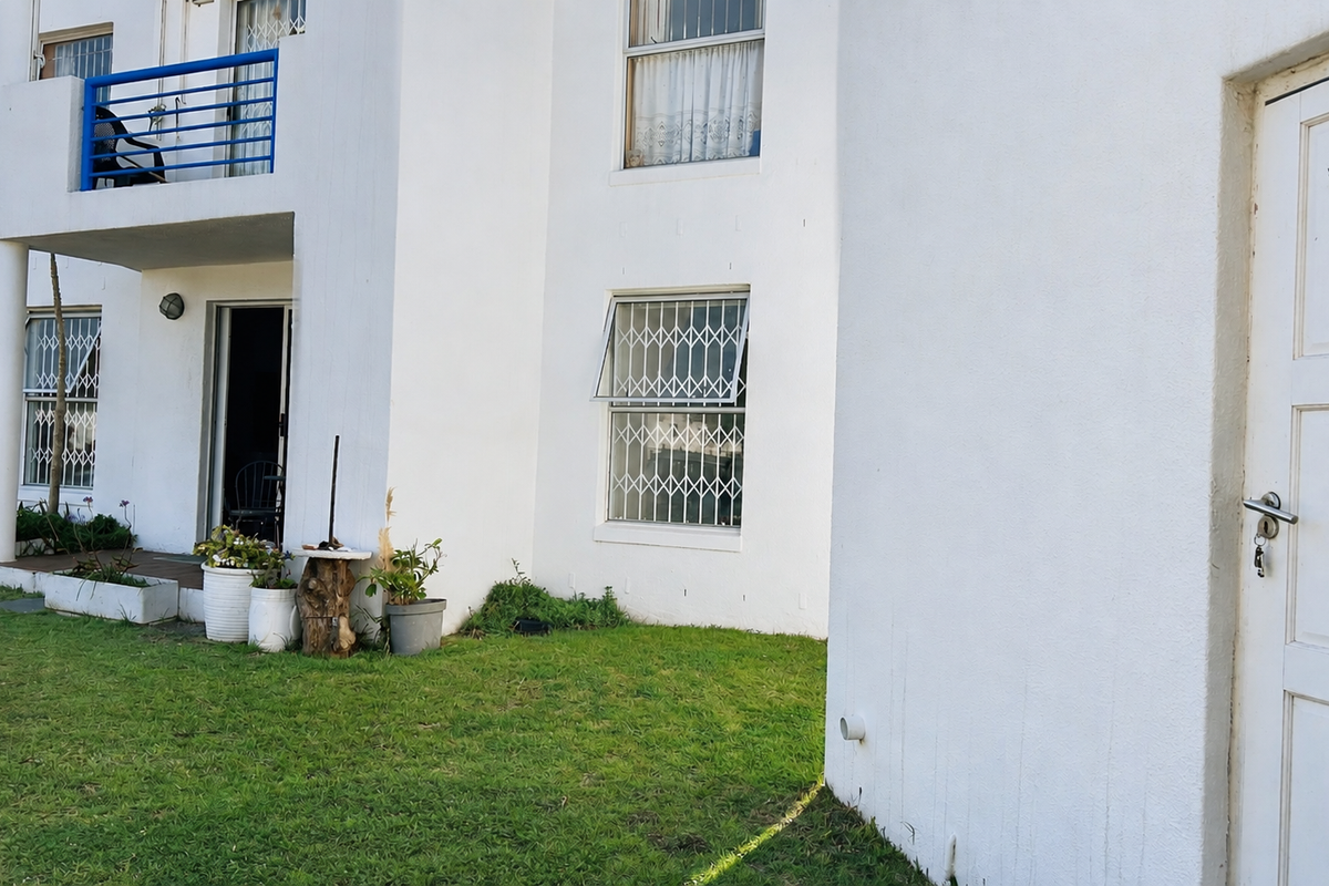 Rear view of the apartment building featuring a small balcony, security-fitted windows, and a private lawn area.