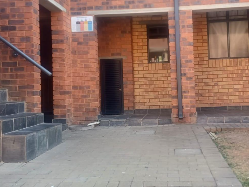 Exterior view of an apartment entrance featuring a face brick facade, paved walkway, and tiled steps with a metal handrail.