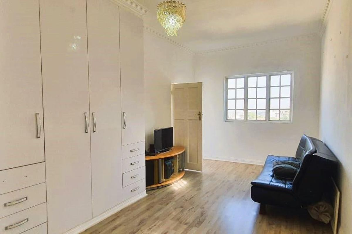 A bedroom featuring extensive built-in white cabinetry with integrated shelving, wood-look flooring, and decorative ceiling cornicing.