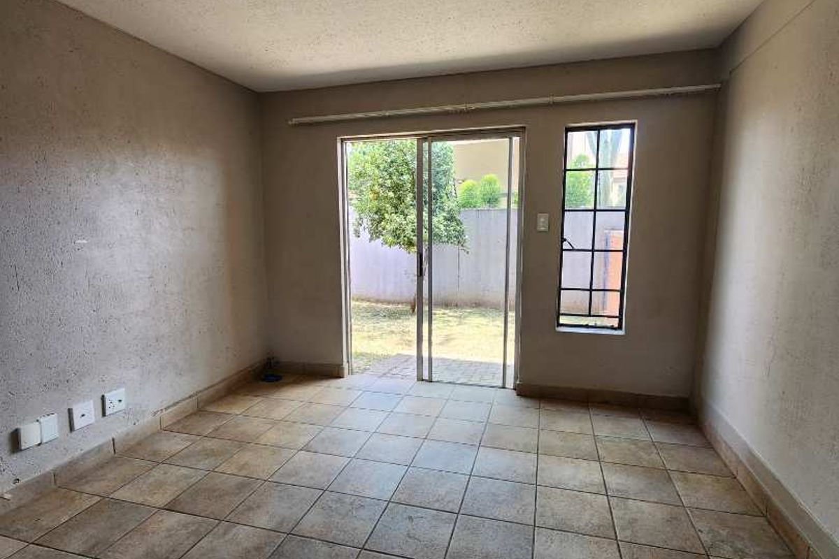 An empty living room featuring tiled flooring, a sliding glass door leading to the exterior, and a single window providing natural light.