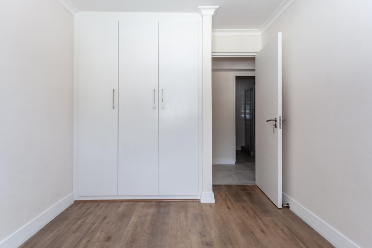A bright bedroom featuring built-in white cabinetry, wood-look flooring, and a modern interior door leading to an adjacent space.