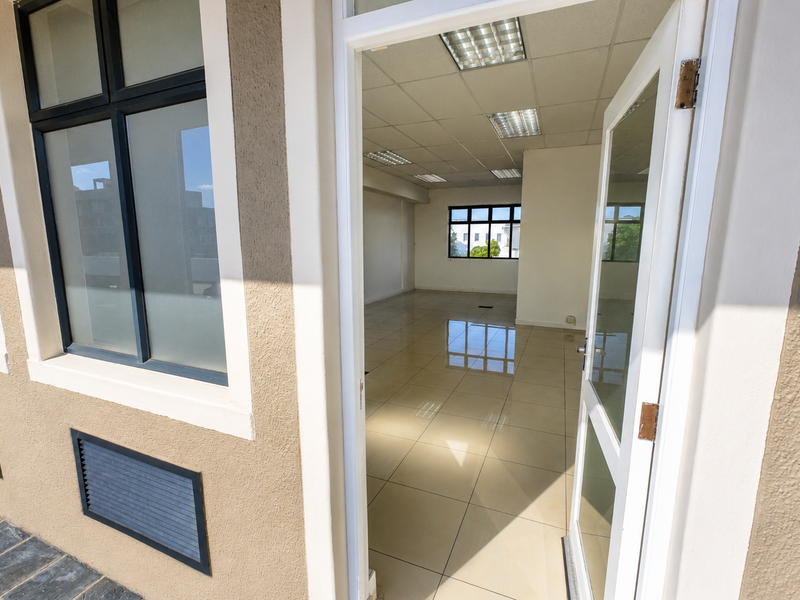 A bright, vacant office space featuring polished tiled flooring, a suspended ceiling with recessed lighting, and large windows providing ample natural light.