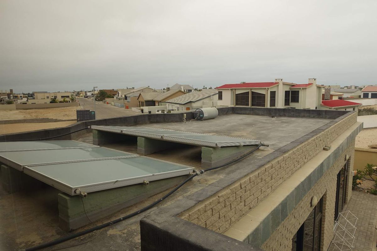 Elevated view of a flat roof featuring solar water heating panels and a geyser, overlooking a residential neighborhood.