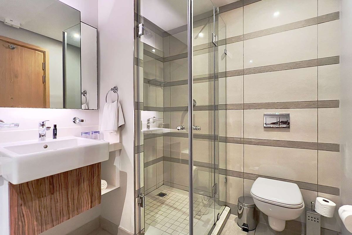 Modern bathroom featuring a glass-enclosed shower, wall-mounted toilet with chrome flush plate, and a contemporary vanity unit with integrated mirror.