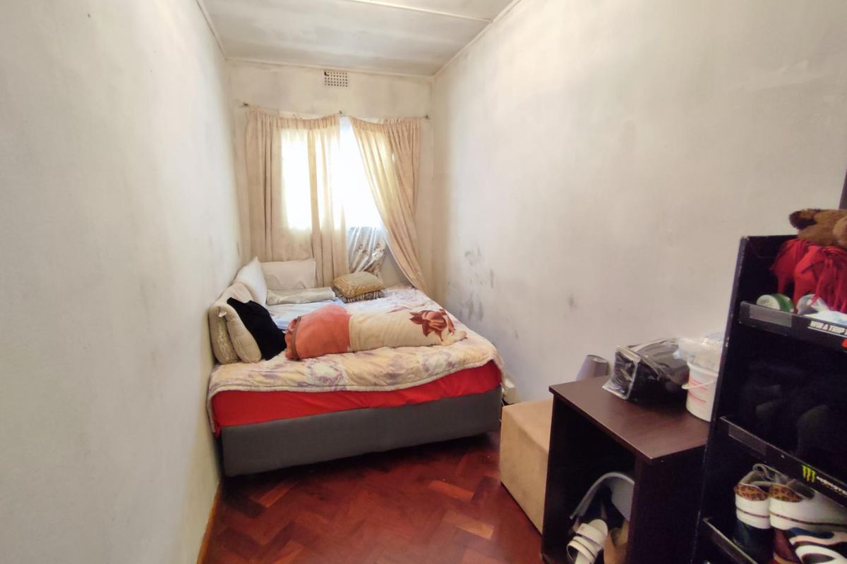 A compact bedroom featuring classic parquet flooring and a window with natural light, requiring cosmetic updates to the wall finishes.