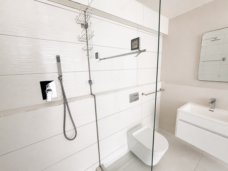 Modern bathroom featuring a wall-mounted toilet, floating vanity, and a glass-enclosed shower area with contemporary white tiled finishes.