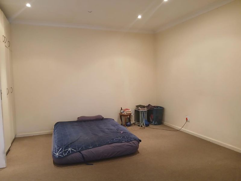 A spacious bedroom featuring neutral walls, carpeted flooring, built-in cupboards, and recessed downlighting, offering a blank canvas for personalization.