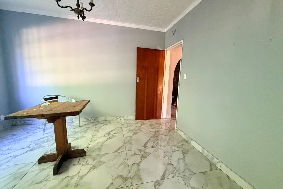 A bright, empty living area featuring modern marble-look floor tiles, a classic wooden door, and a traditional chandelier.