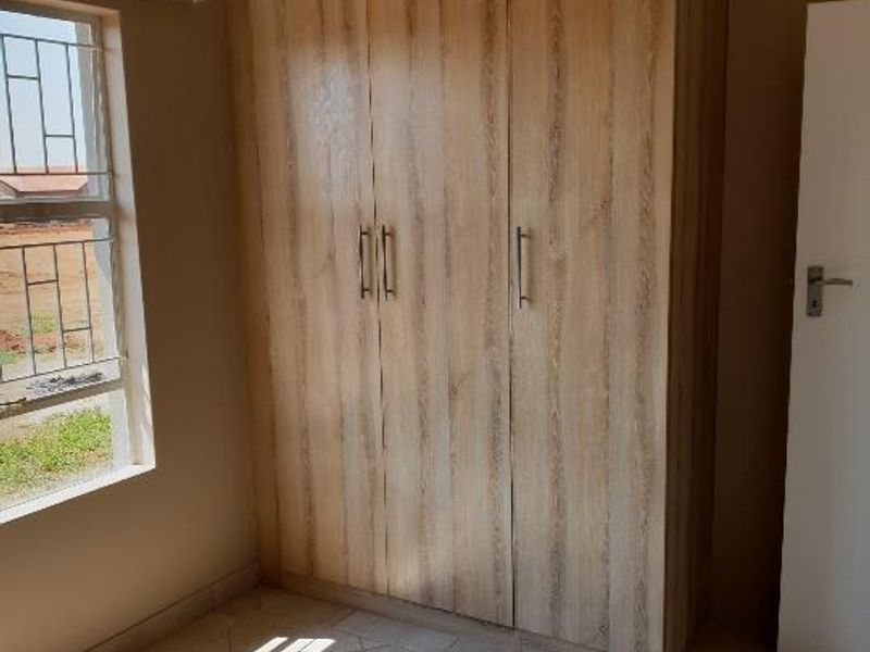 A bright bedroom featuring light wood-finish built-in wardrobes, tiled flooring, and a window with security bars.