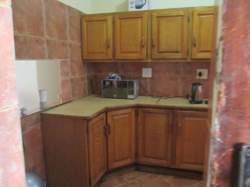A compact kitchen featuring traditional wooden cabinetry, laminate countertops, and tiled wall finishes, offering a functional layout in need of modernization.