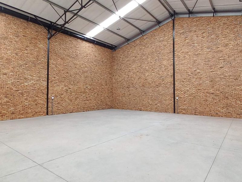 Spacious industrial warehouse unit featuring high ceilings with exposed steel trusses, durable concrete flooring, and attractive face-brick walls.