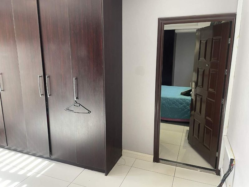 Bedroom featuring dark wood built-in wardrobes, tiled flooring, and a view into an adjacent room through a panel door.