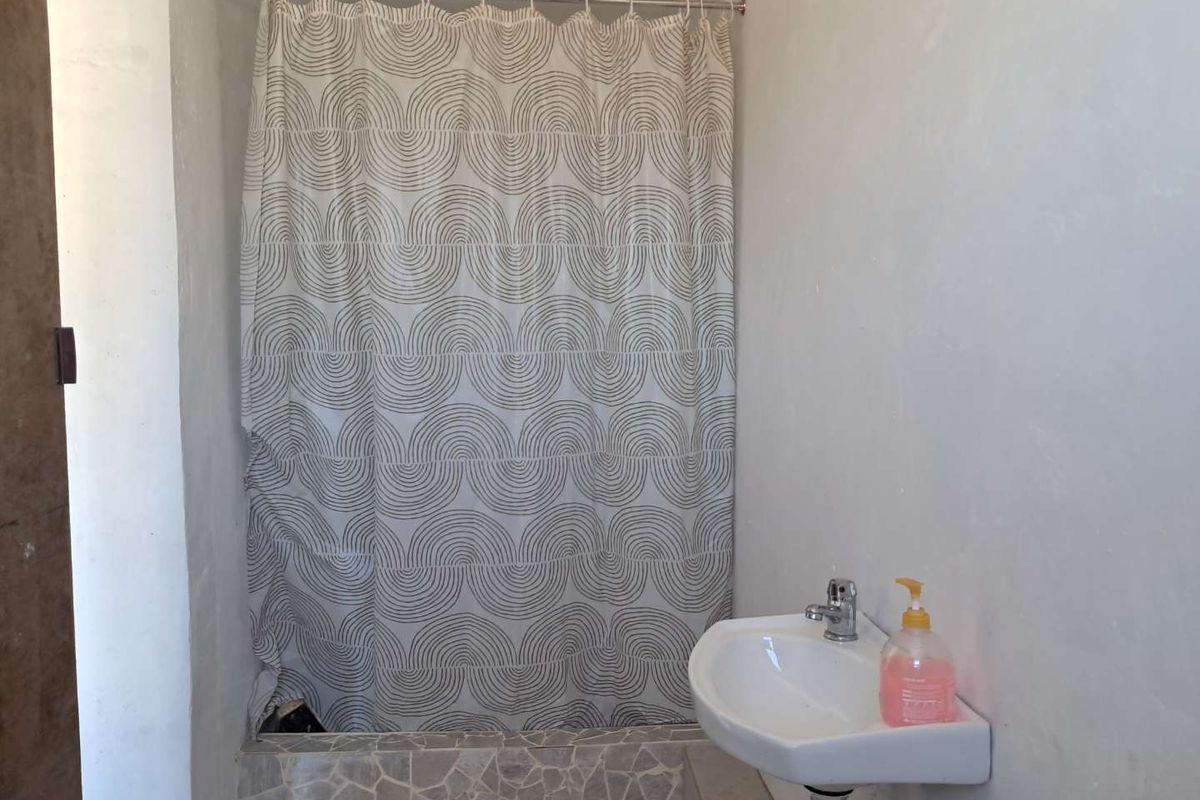 A compact bathroom featuring a wall-mounted basin and a shower area enclosed by a curtain, showcasing basic finishes and functional fixtures.