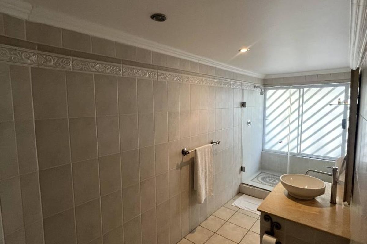 A functional bathroom featuring a walk-in shower with glass enclosure, a stone-topped vanity with vessel sink, and neutral wall and floor tiling.