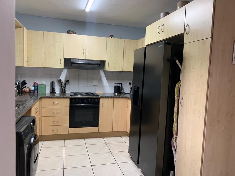 Functional kitchen featuring light wood cabinetry, granite countertops, tiled backsplash, and integrated cooking appliances with tiled flooring.