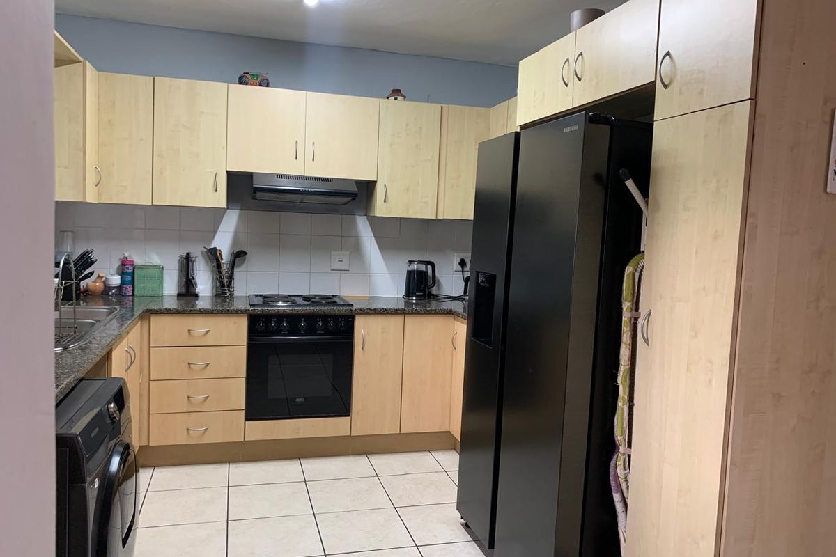 Functional kitchen featuring light wood cabinetry, granite countertops, tiled backsplash, and integrated cooking appliances with tiled flooring.