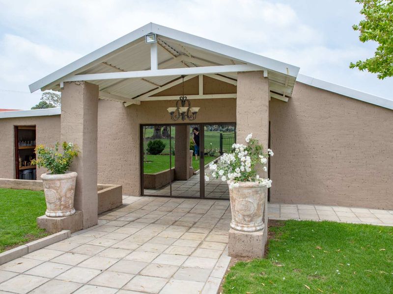 A well-maintained farm property entrance featuring a covered walkway, stucco facade, and sliding glass doors leading into the main building.
