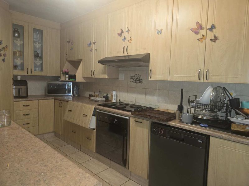 A dated kitchen featuring light wood-finish cabinetry, laminate countertops, built-in oven, gas hob, and tiled flooring, requiring cosmetic updates to modernize the space.