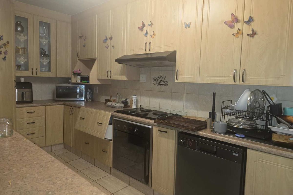 A dated kitchen featuring light wood-finish cabinetry, laminate countertops, built-in oven, gas hob, and tiled flooring, requiring cosmetic updates to modernize the space.