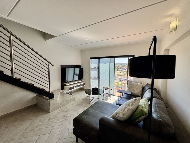 Modern living room featuring herringbone tile flooring, a sleek staircase with stainless steel balustrade, and large sliding glass doors leading to a balcony.