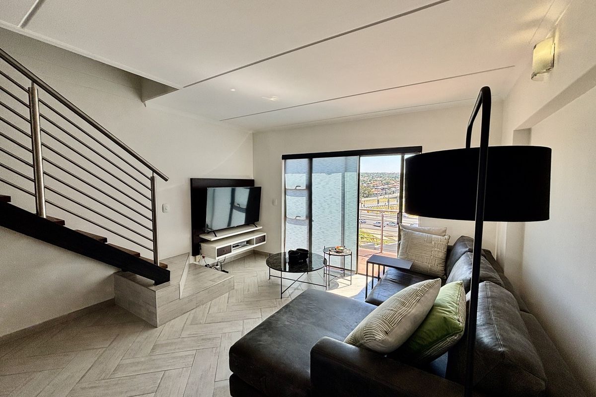 Modern living room featuring herringbone tile flooring, a sleek staircase with stainless steel balustrade, and large sliding glass doors leading to a balcony.