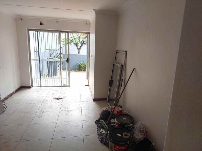 An empty living room featuring tiled flooring and a sliding glass door leading to an outdoor area, requiring minor cosmetic updates.