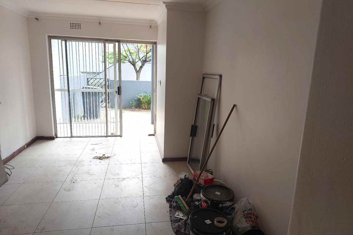 An empty living room featuring tiled flooring and a sliding glass door leading to an outdoor area, requiring minor cosmetic updates.