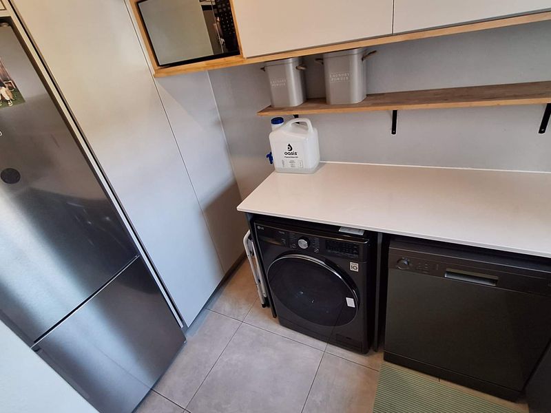 A modern, functional laundry area featuring built-in cabinetry, stone countertops, open shelving, and tiled flooring, designed for efficient utility and storage.