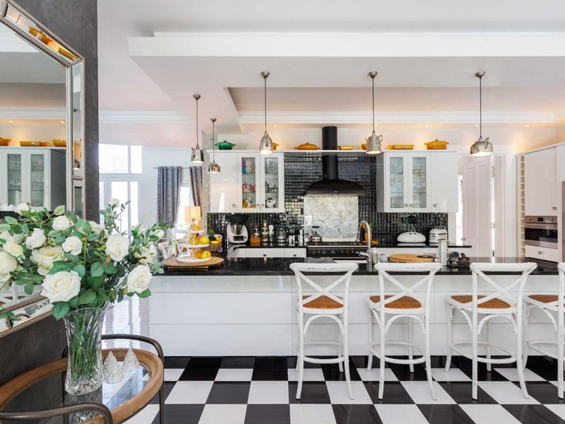 A modern, high-contrast kitchen featuring white cabinetry, black granite countertops, a striking black mosaic backsplash, and a classic checkerboard tiled floor.
