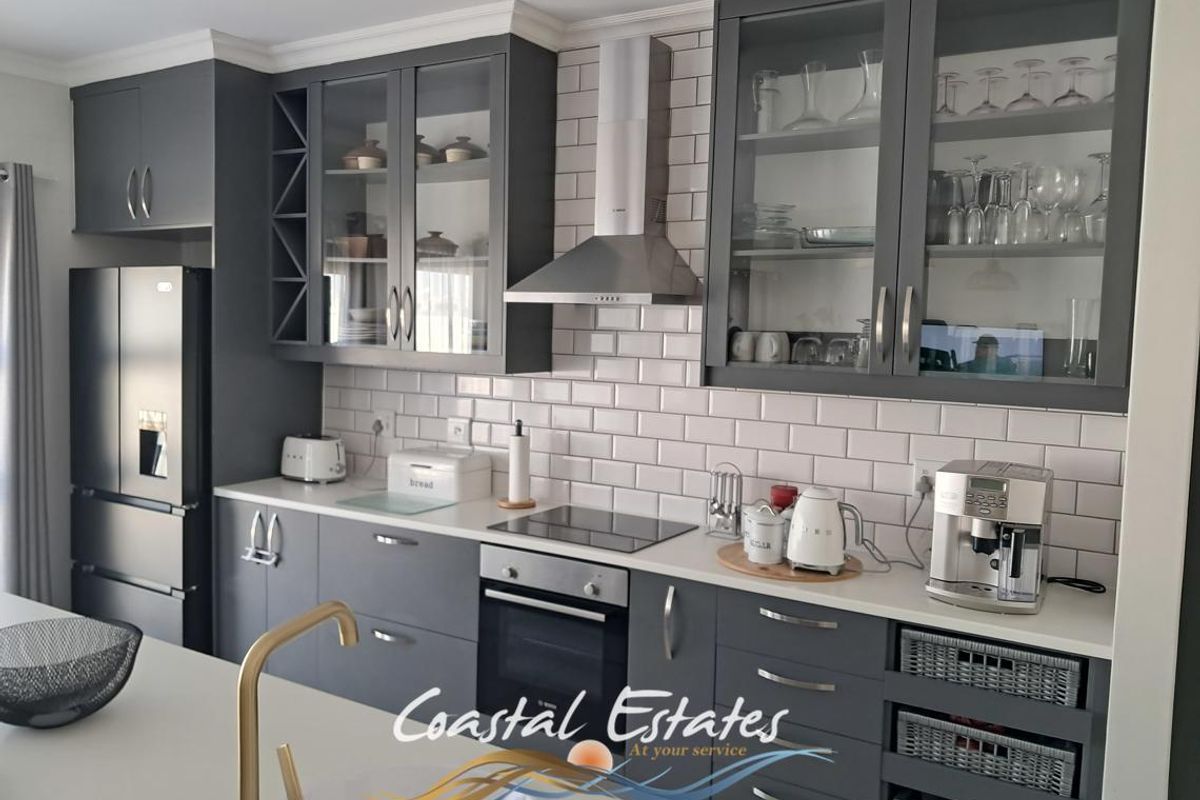 Modern kitchen featuring dark grey cabinetry, subway tile backsplash, stainless steel appliances, and elegant brass fixtures with ample storage and workspace.