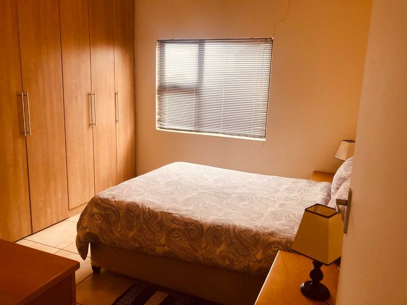 A functional bedroom featuring built-in wooden cupboards and a window with venetian blinds, offering a comfortable and practical living space.