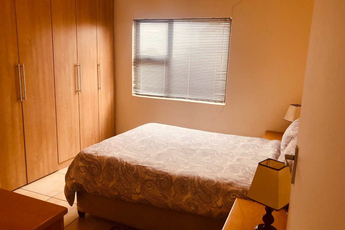 A functional bedroom featuring built-in wooden cupboards and a window with venetian blinds, offering a comfortable and practical living space.