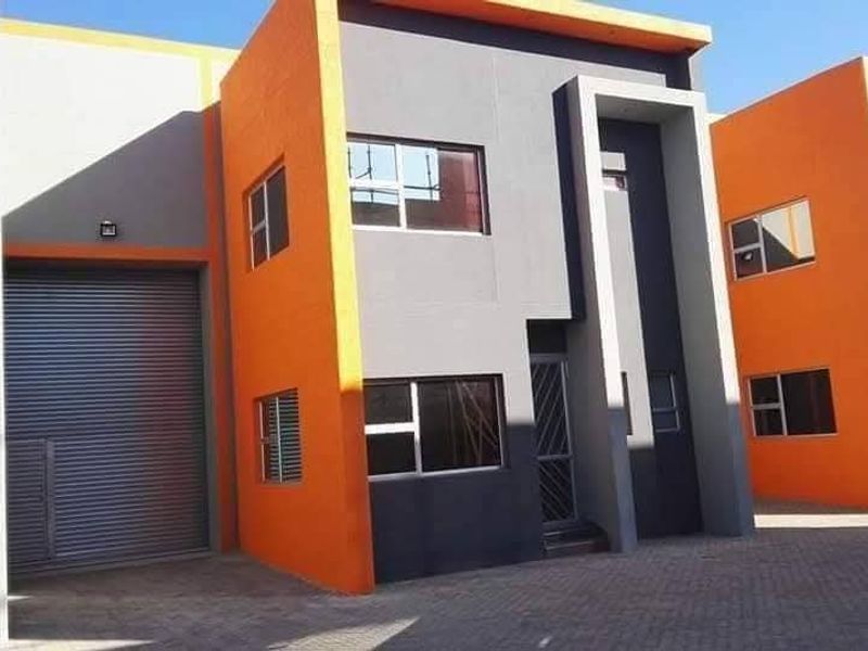 Modern industrial unit featuring a bold orange and grey facade, large roller shutter door, and paved access area.