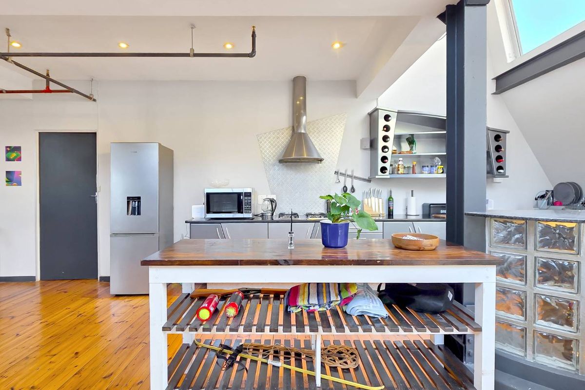 Modern industrial-style kitchen featuring hardwood floors, exposed structural elements, stainless steel extractor fan, and a unique glass block partition.