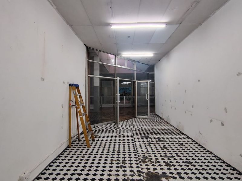 Empty retail entry space featuring a glass storefront, checkered tile flooring, and fluorescent lighting, currently requiring cosmetic repairs and refurbishment.