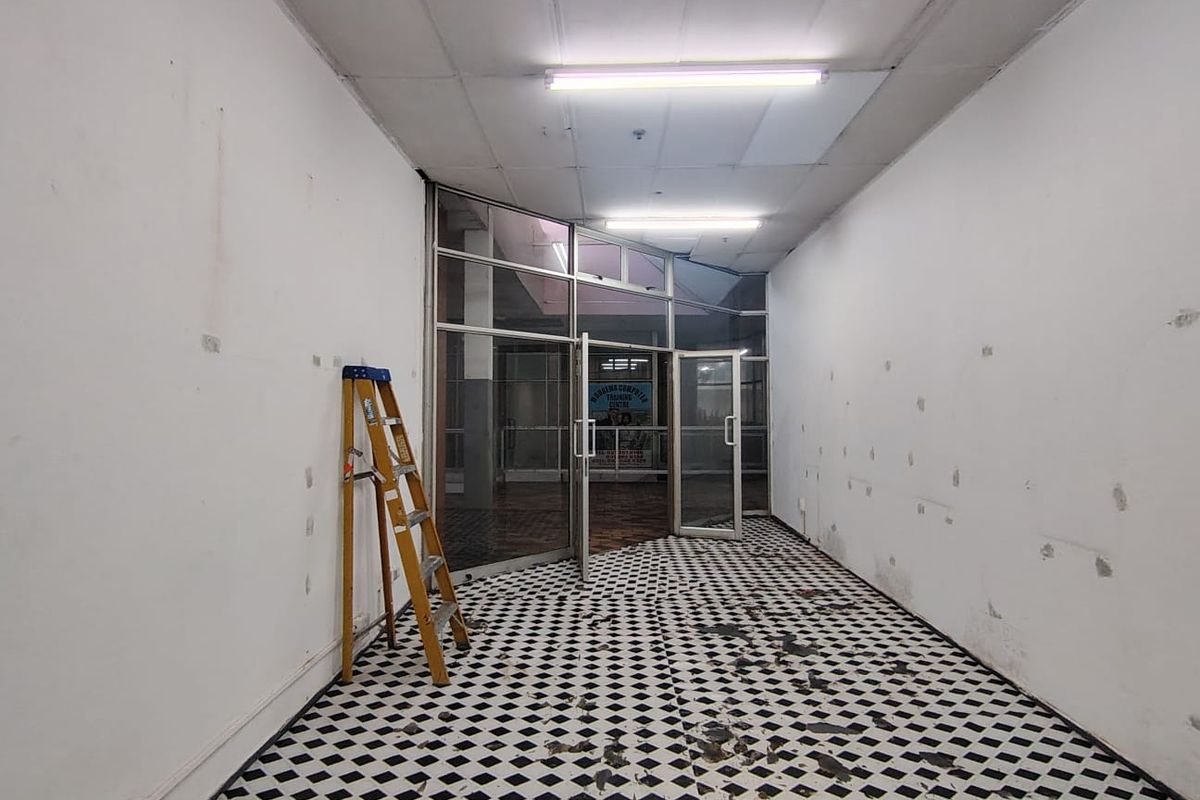 Empty retail entry space featuring a glass storefront, checkered tile flooring, and fluorescent lighting, currently requiring cosmetic repairs and refurbishment.