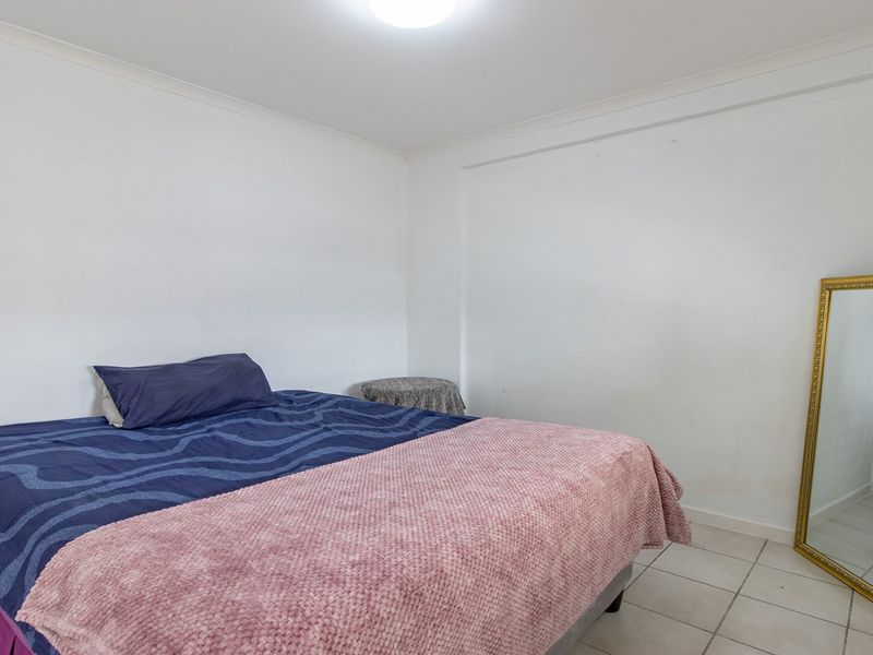A simple bedroom featuring tiled flooring and neutral white walls, offering a blank canvas for personalization.