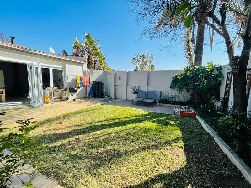 A private rear garden featuring a wooden deck, paved patio area, and a well-maintained lawn enclosed by a perimeter boundary wall.