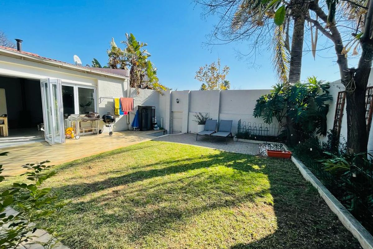 A private rear garden featuring a wooden deck, paved patio area, and a well-maintained lawn enclosed by a perimeter boundary wall.