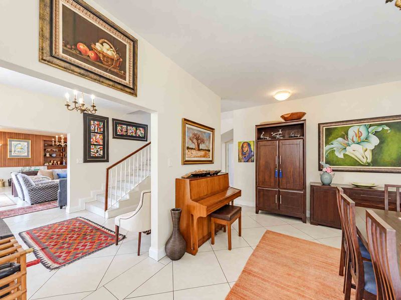 An open-plan living and dining area featuring tiled flooring, a central staircase with a wooden banister, and neutral wall finishes.