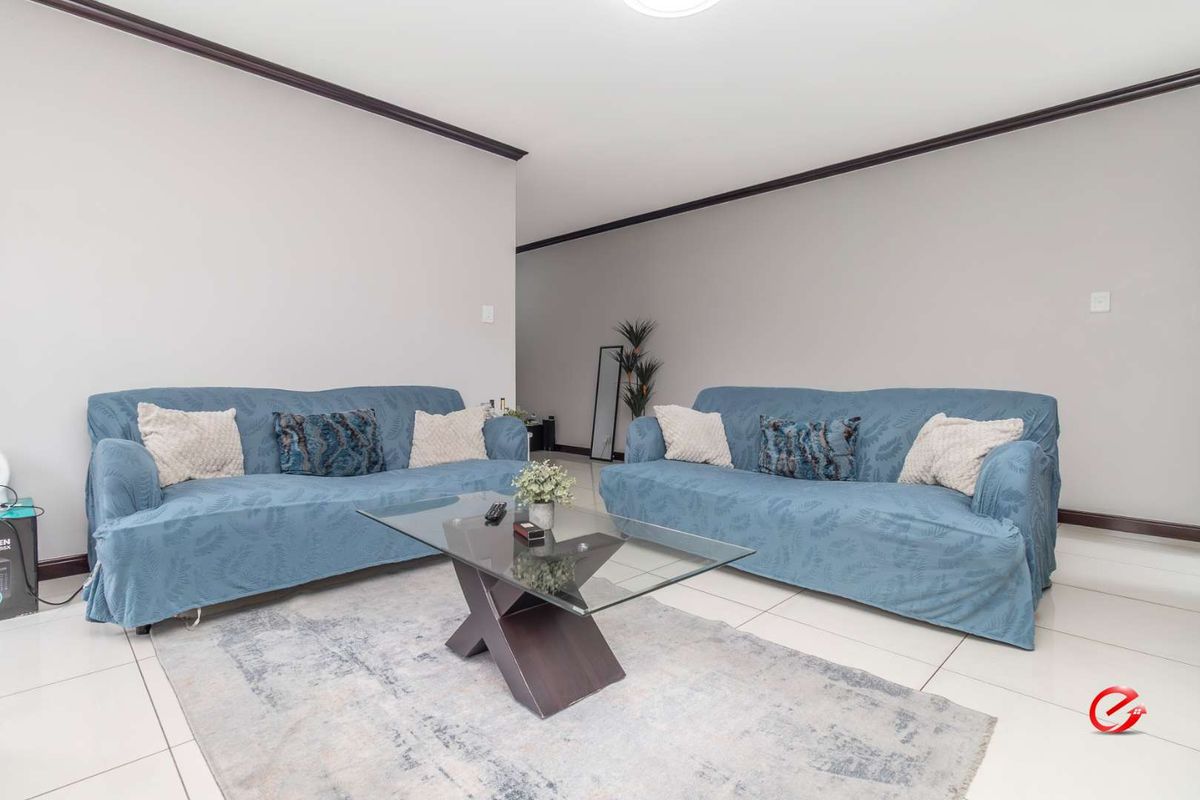 A spacious living room featuring neutral wall tones, dark crown molding, and polished floor tiles, providing a clean and versatile living space.