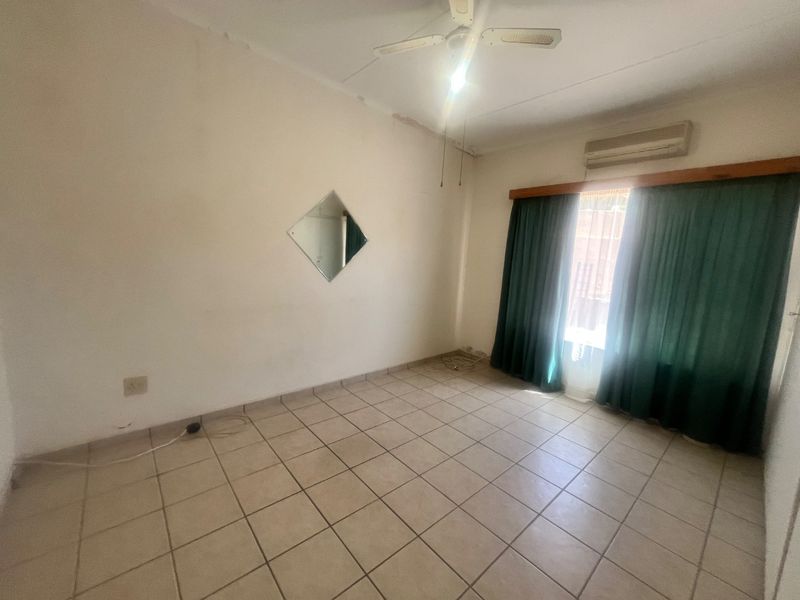 An empty bedroom featuring tiled flooring, a ceiling fan, and a wall-mounted air conditioning unit, ready for a fresh update.