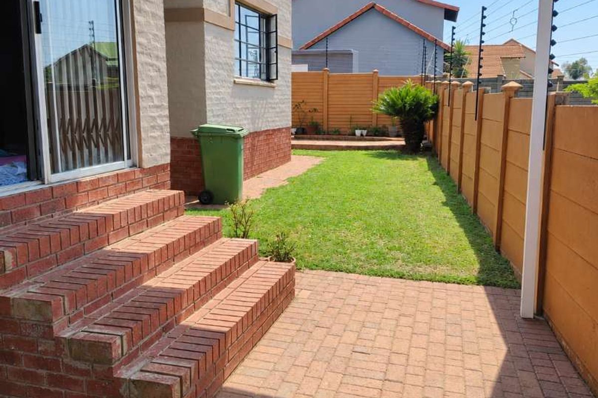 Rear exterior view of the townhouse featuring a paved patio area, brick steps leading to a sliding door, and a private garden with perimeter fencing.