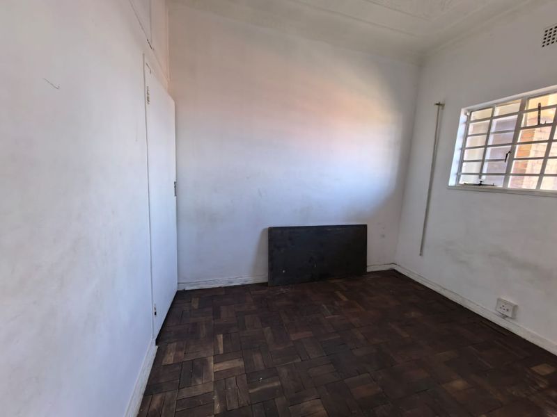 An empty bedroom featuring original parquet flooring, white walls, and a window fitted with security bars.