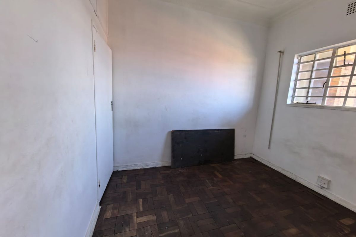 An empty bedroom featuring original parquet flooring, white walls, and a window fitted with security bars.