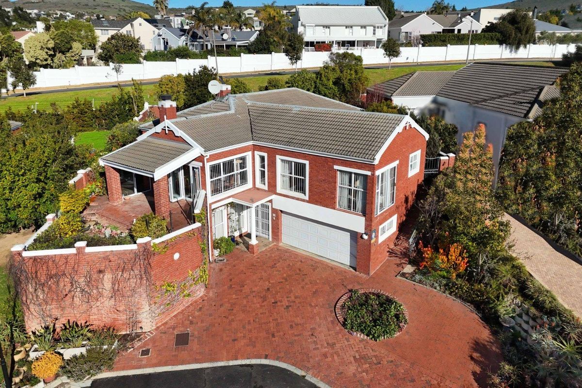 Aerial view of a double-story brick townhouse featuring a paved driveway, double garage, and a covered patio area within a residential estate.