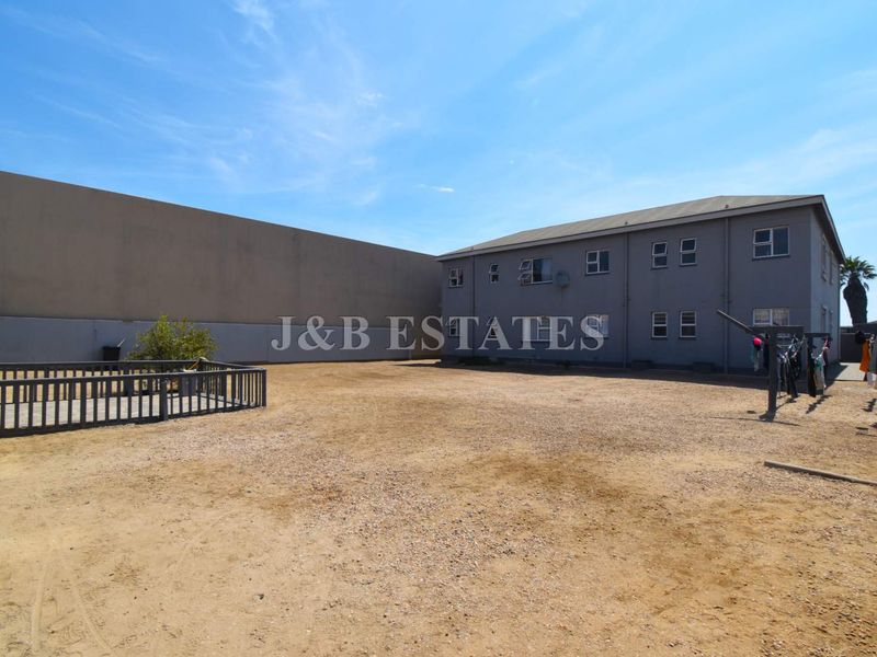 Rear exterior view of the property featuring a large, unpaved open yard area adjacent to the building structure.