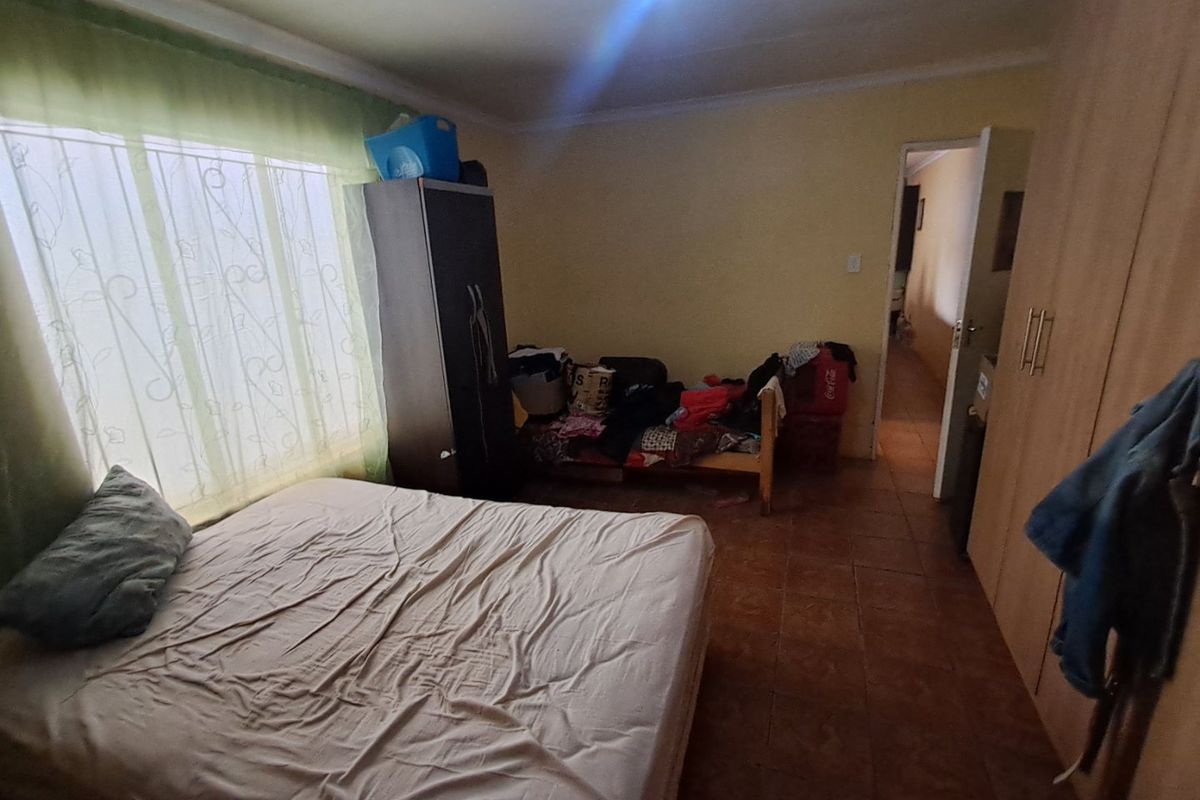 A bedroom featuring tiled flooring and built-in cupboards, offering a functional space with natural light from the window.
