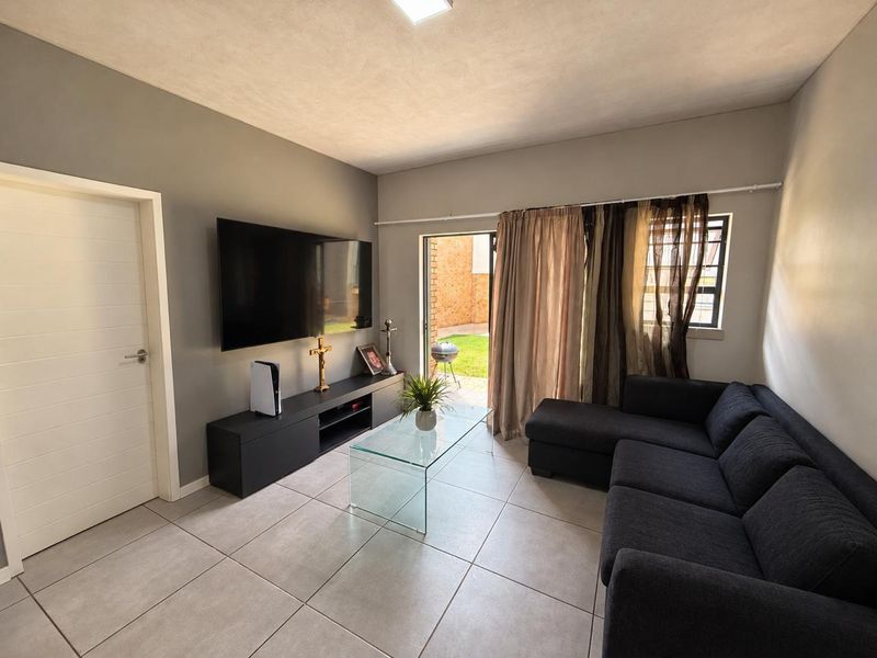 A well-maintained living room featuring neutral tiled flooring and direct access to an outdoor patio area through a sliding glass door.